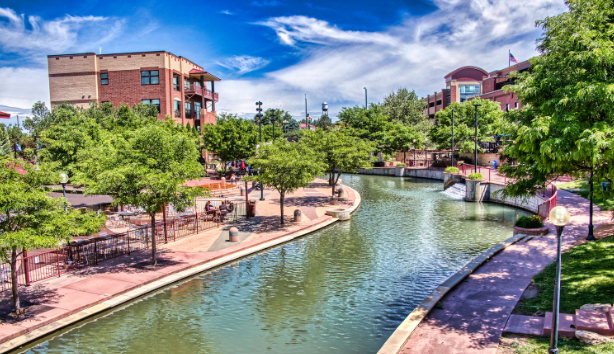 Pueblo downtown shows serene river channels flaked by walkways with seating. Shady trees line the walkway provided with accessible features including raised strips on the pavement, adequate lighting, etc.